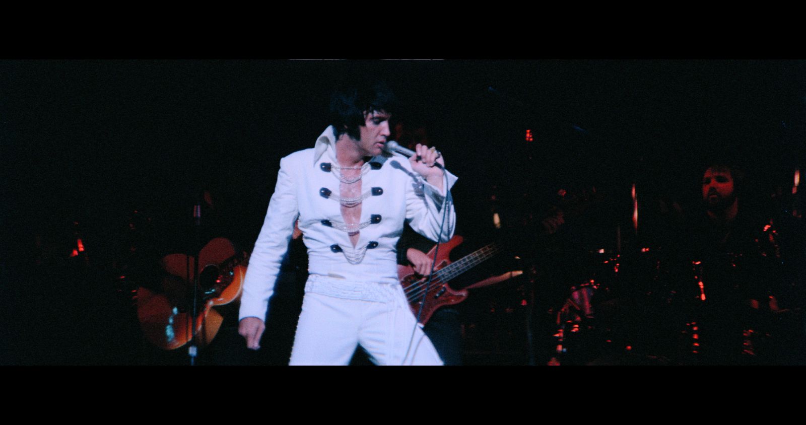 Elvis Presley performs in concert wearing a whte jumpsuit.