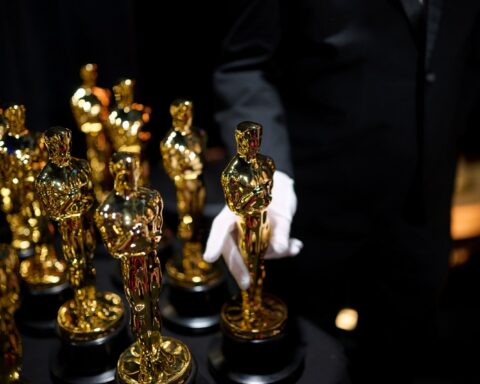 Two rows of Oscar statuettes stand backstage at the 2025 Academy Awards. A pair of hands in white gloves holds one statuette.