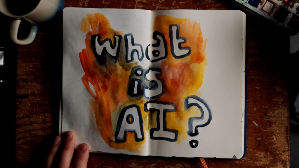 An open notebook contains the words What is AI? written in bubble letters with flames around them.