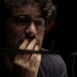 Filmmaker Daniel Roher is pictures in close-up. His hand is touching his face and he looks pensive while listening to an interviewee.