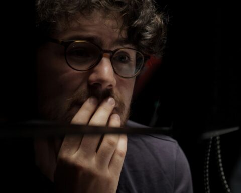 Filmmaker Daniel Roher is pictures in close-up. His hand is touching his face and he looks pensive while listening to an interviewee.