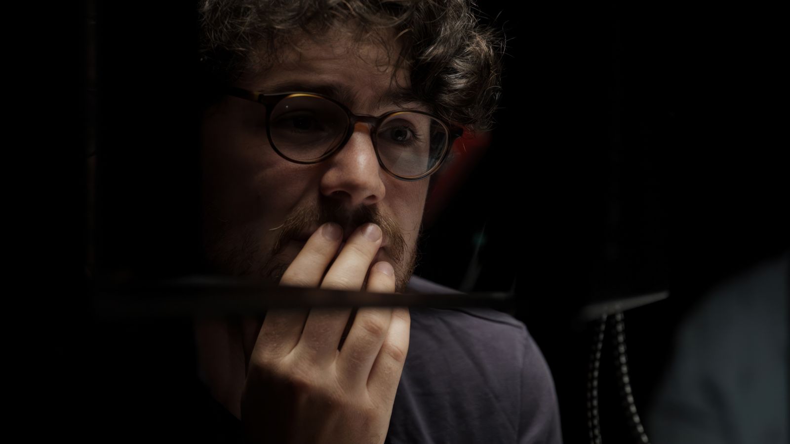 Filmmaker Daniel Roher is pictures in close-up. His hand is touching his face and he looks pensive while listening to an interviewee.
