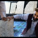 An Afghan man kneels down and examines a white marble panel with intricate carvings.
