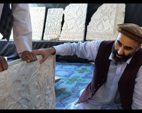 An Afghan man kneels down and examines a white marble panel with intricate carvings.