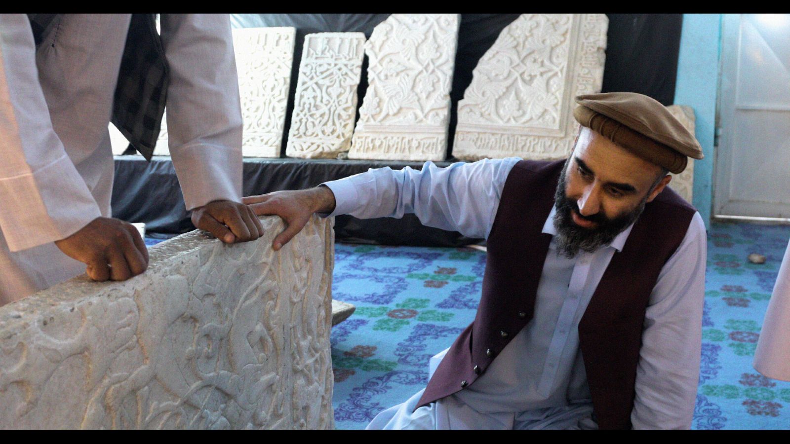 An Afghan man kneels down and examines a white marble panel with intricate carvings.