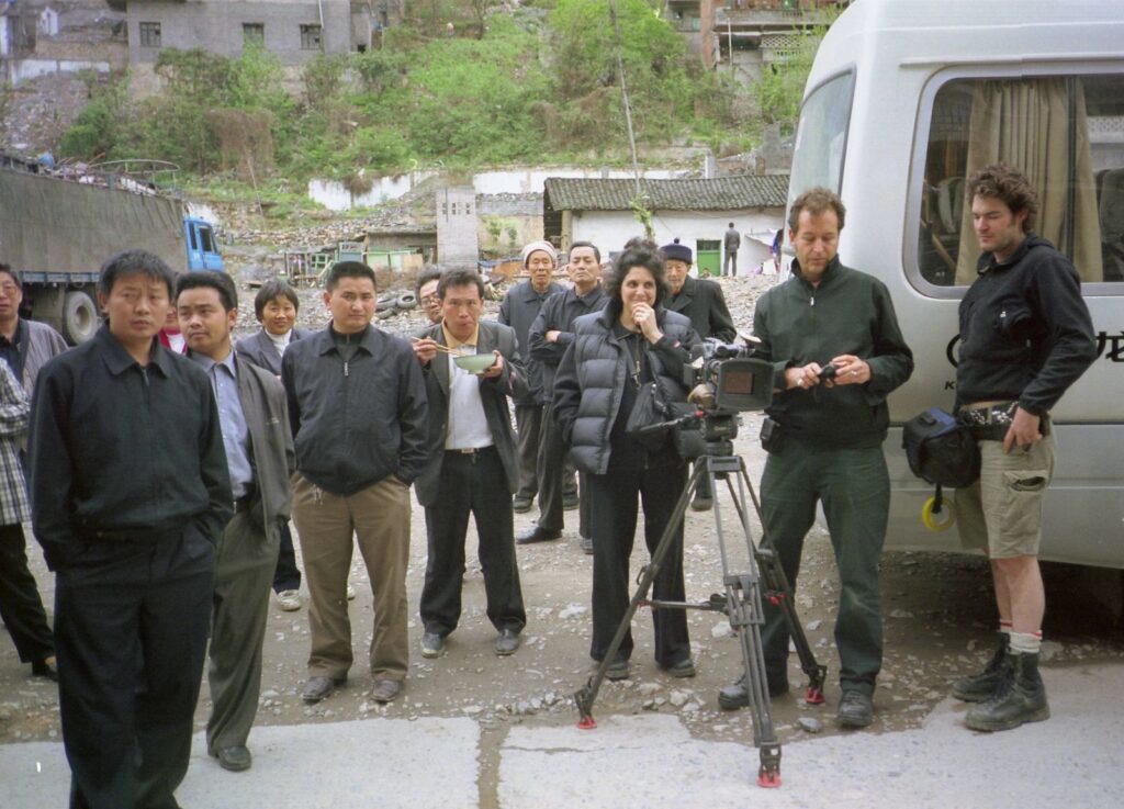 Jennifer Baichwal (director, at centre), Peter Mettler (director of photography, right) John Price (camera assistant, at far right), and crowd in Wushan, China, during production of Manufactured Landscapes (2006). [Credit:] Mercury Filmworks / Mongrel Media