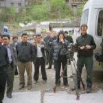Jennifer Baichwal (director, at centre), Peter Mettler (director of photography, right) John Price (camera assistant, at far right), and crowd in Wushan, China, during production of Manufactured Landscapes (2006). [Credit:] Mercury Filmworks / Mongrel Media