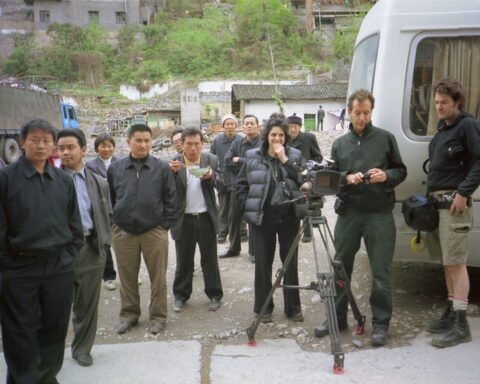 Jennifer Baichwal (director, at centre), Peter Mettler (director of photography, right) John Price (camera assistant, at far right), and crowd in Wushan, China, during production of Manufactured Landscapes (2006). [Credit:] Mercury Filmworks / Mongrel Media