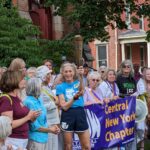 79-year-old runner Katrine Switzer holds the Olympic torch. She is surrounded by an enthusiastic crowd.