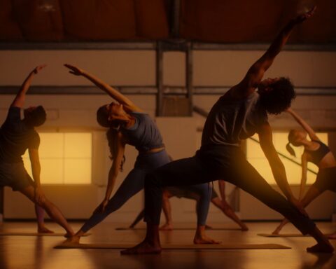A group of people perform yoga stretches. The are pictured in a golden hue.