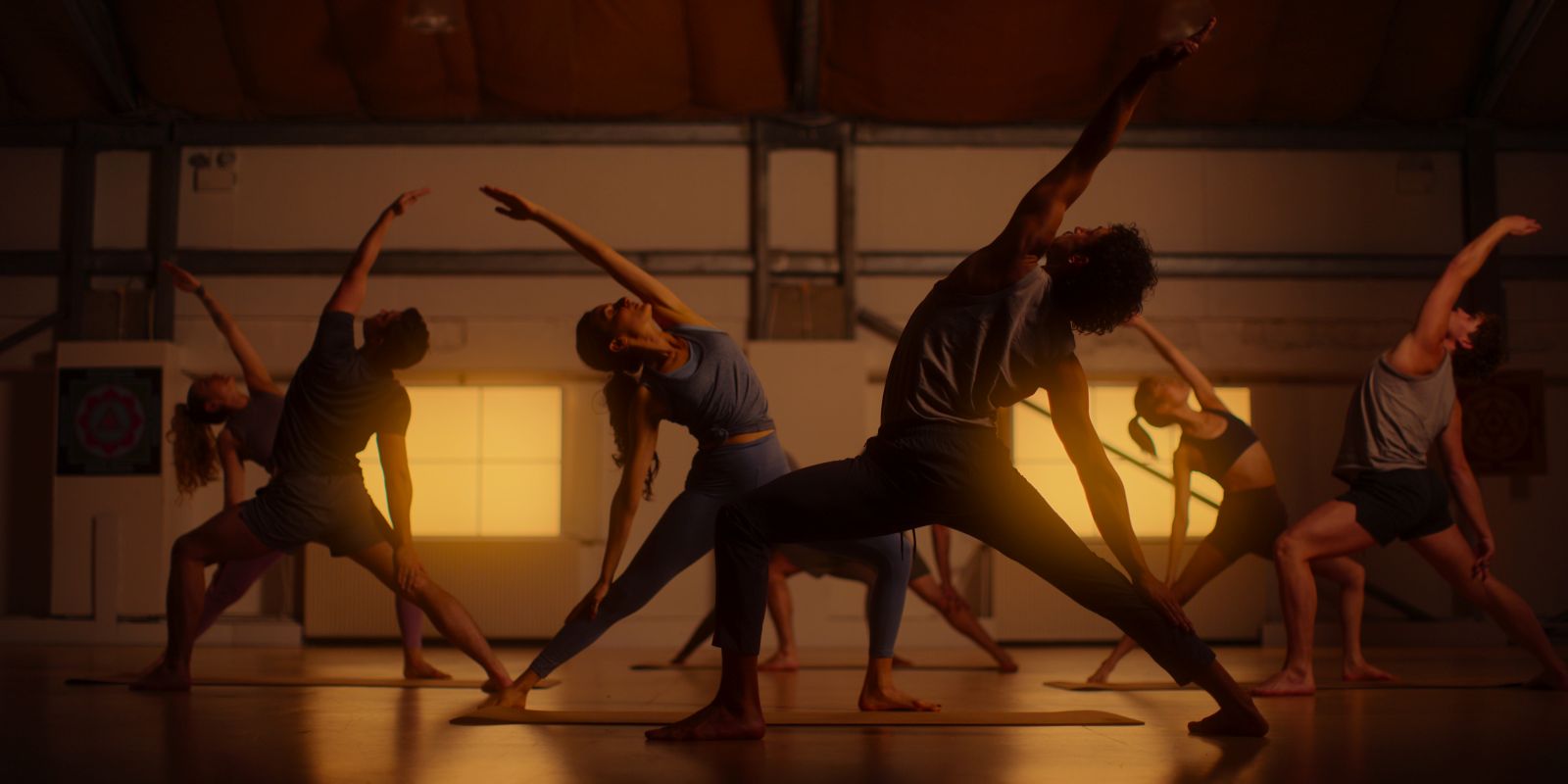 A group of people perform yoga stretches. The are pictured in a golden hue.