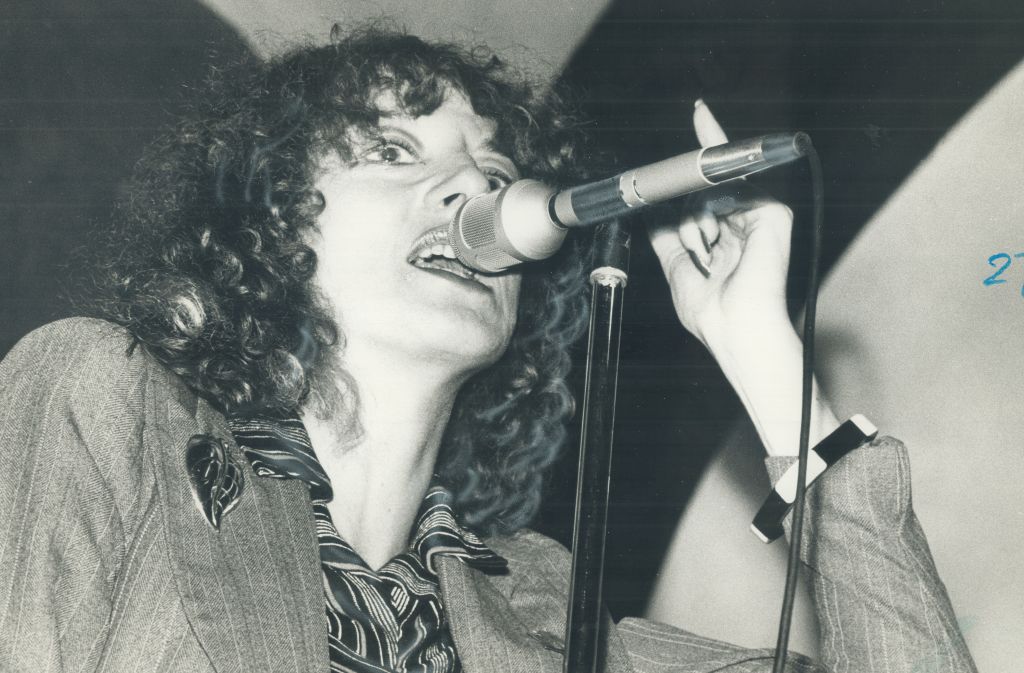 A black and white photo of Carole Pope singing behind a microphone