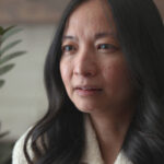 Jin Kim Diep is a Chinese-Canadian woman with black hair. She is pictured in close-up giving an interview. She is facing the camera and wearing a white collared short. There is a plant in the background.