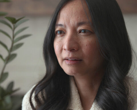 Jin Kim Diep is a Chinese-Canadian woman with black hair. She is pictured in close-up giving an interview. She is facing the camera and wearing a white collared short. There is a plant in the background.