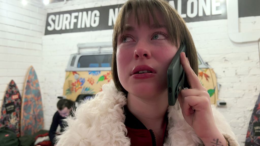 Journalist Ksenia Mironova is seen in close-up. She is speaking on a cell phone and has an anxious expression.