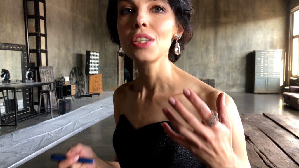 A close up of journalist Anna Nemzer. She is a white Russian woman with short brown hair. She is wearing a black dress and speaking to the camera with an animated gesture.