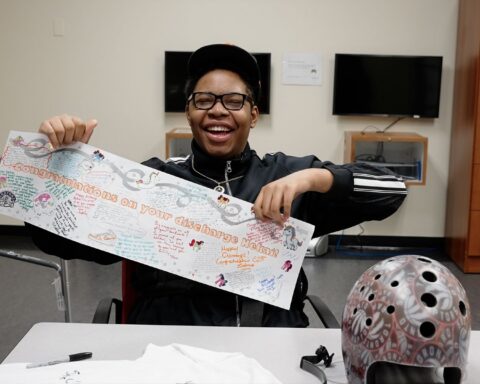 Nekai Foster holds a banner that reads "Congratulations on your discharge, Nekai." He is a young Black man seated a a table. He wears a black track suit, ballcap, and glasses. He is smiling.