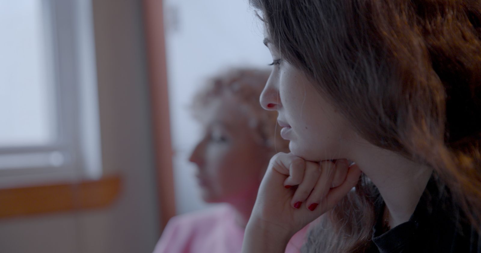 A young woman is pictured in close-up. She is white and has brown hair. Her head rests on her hand beneath her chin and she has a thoughtful look.
