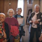 Seven senior citizen stand in a semi-circle facing the camera.