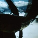 A view down the propeller of an airplane, which is flying over mountains.