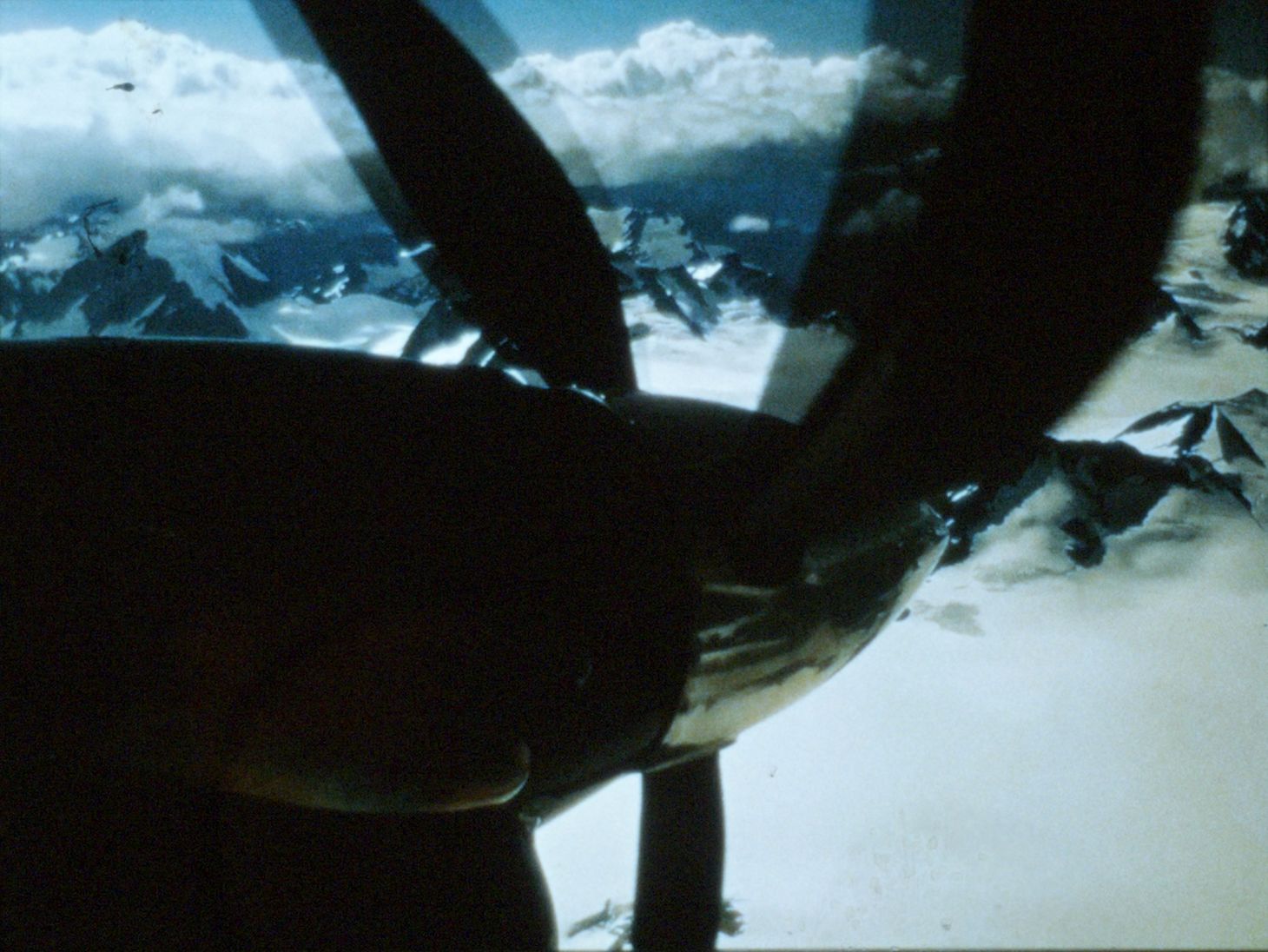 A view down the propeller of an airplane, which is flying over mountains.