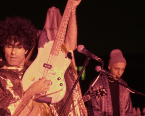 A musician in an Iranian punk bank holds his guitar up in the air.