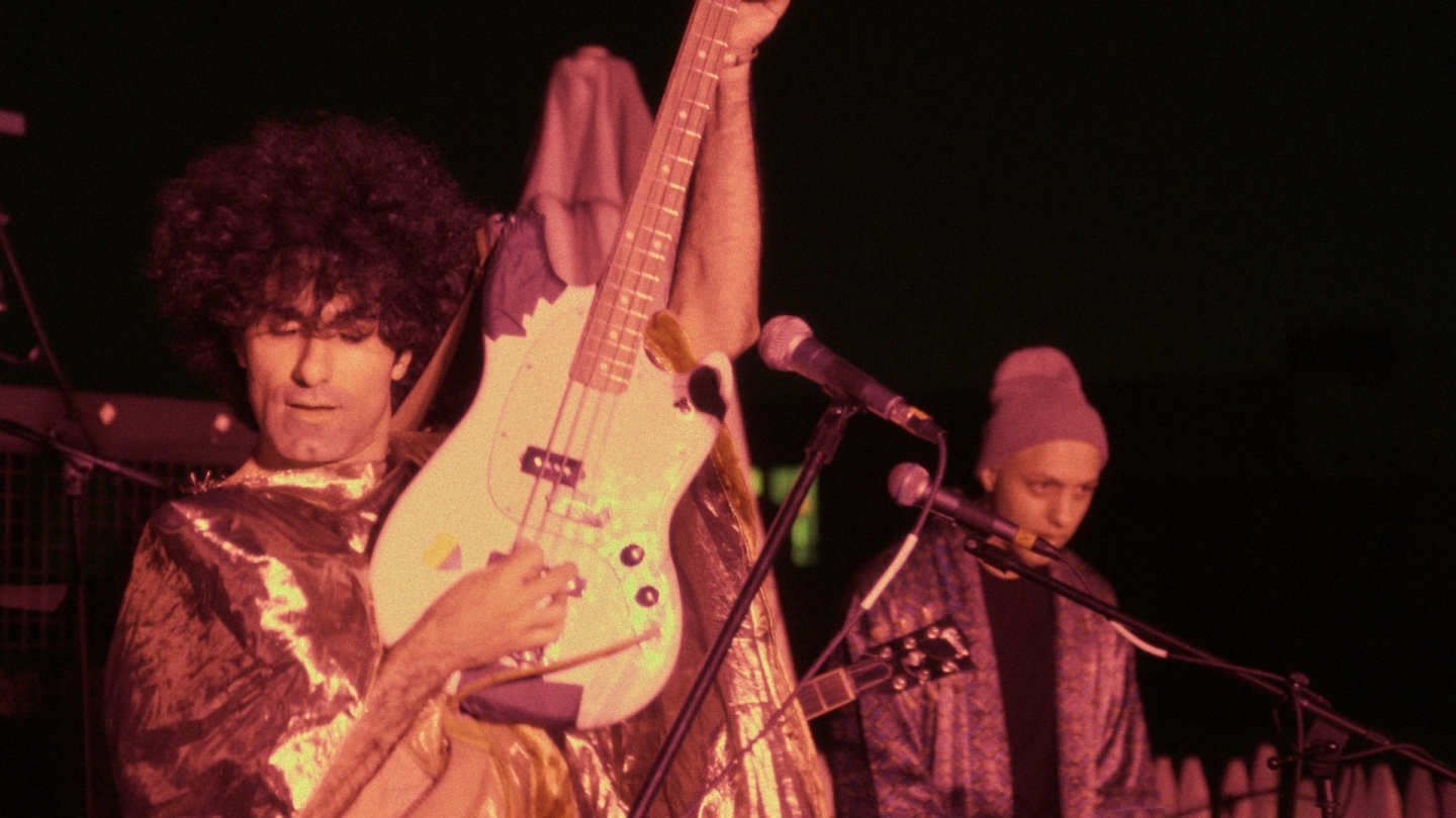 A musician in an Iranian punk bank holds his guitar up in the air.