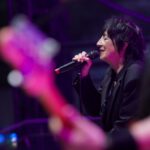 Rocker Carole Pope is views in profile as she sings on stage. A guitarist is in the foreground of the picture.