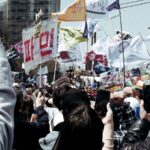 Thousands of South Koreans protest together. They are holding signs and banners.