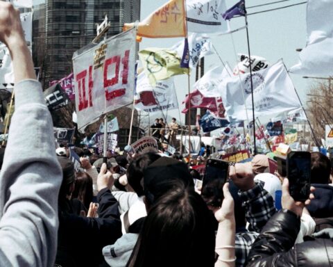 Thousands of South Koreans protest together. They are holding signs and banners.
