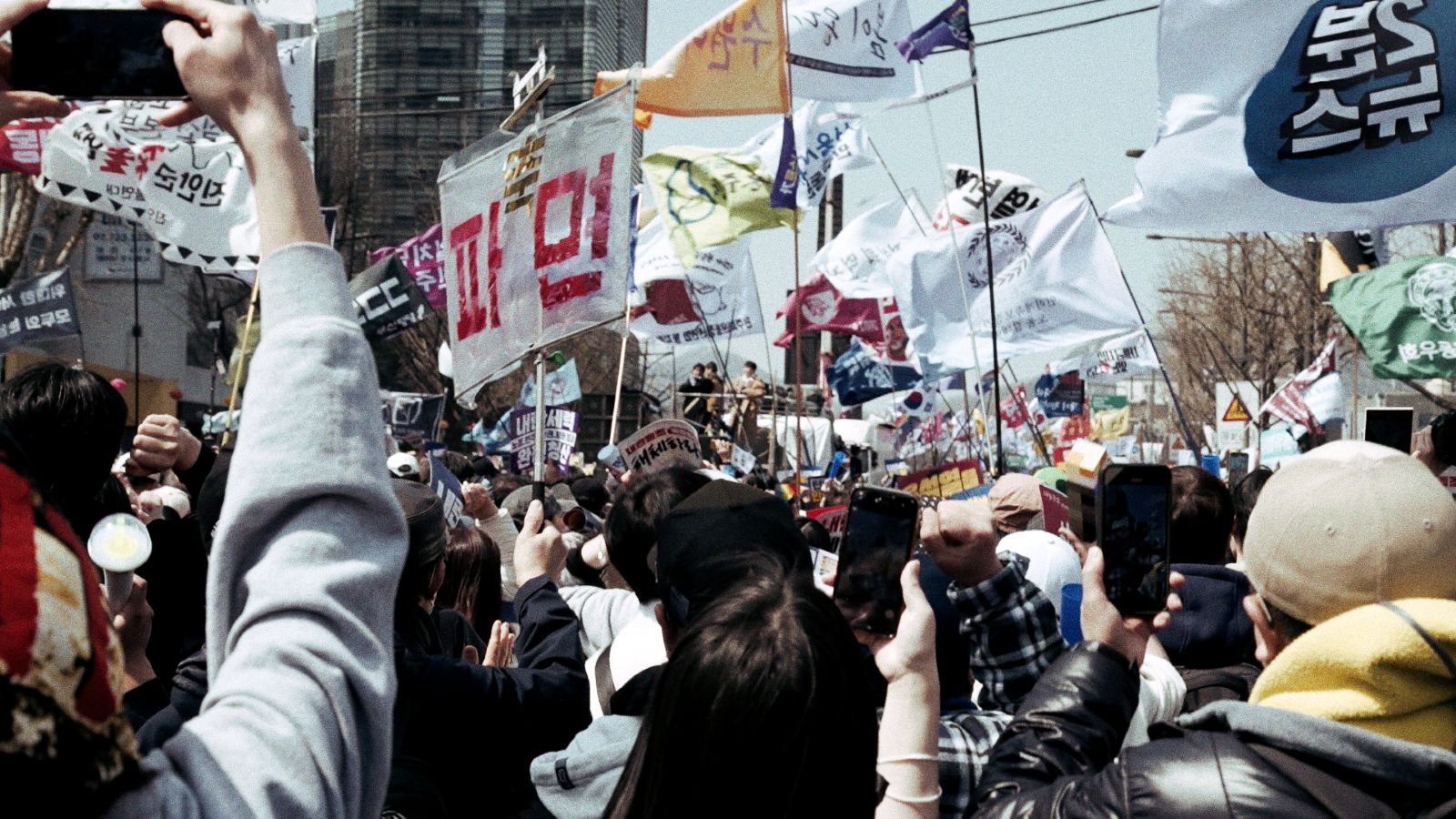 Thousands of South Koreans protest together. They are holding signs and banners.