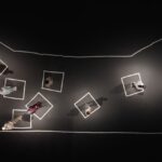 An overhead view of a soundstage covered in a black canvas as nine Palestinians stand in white square outlines that represent their former neighbourhoods and homes.