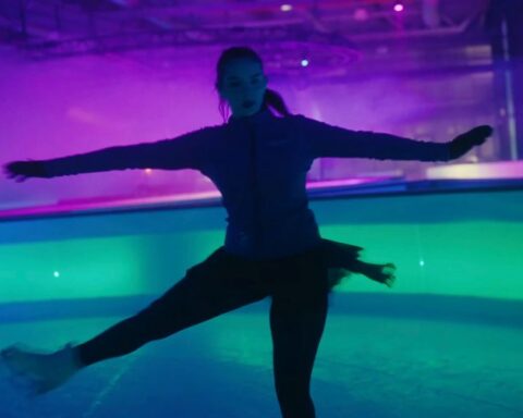 A skater does a pirouette while the scene around her is a dazzling mix of purple, green, and blue light