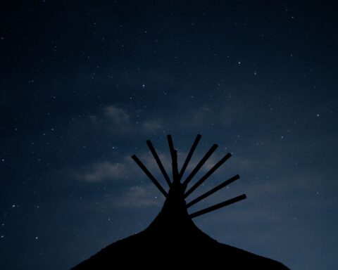A silhouette of the top of a teepee against the backdrop of a starry night.