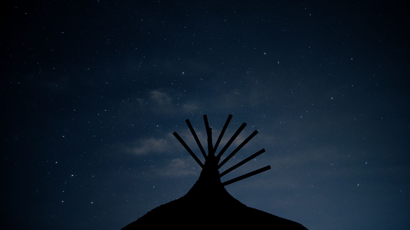 A silhouette of the top of a teepee against the backdrop of a starry night.