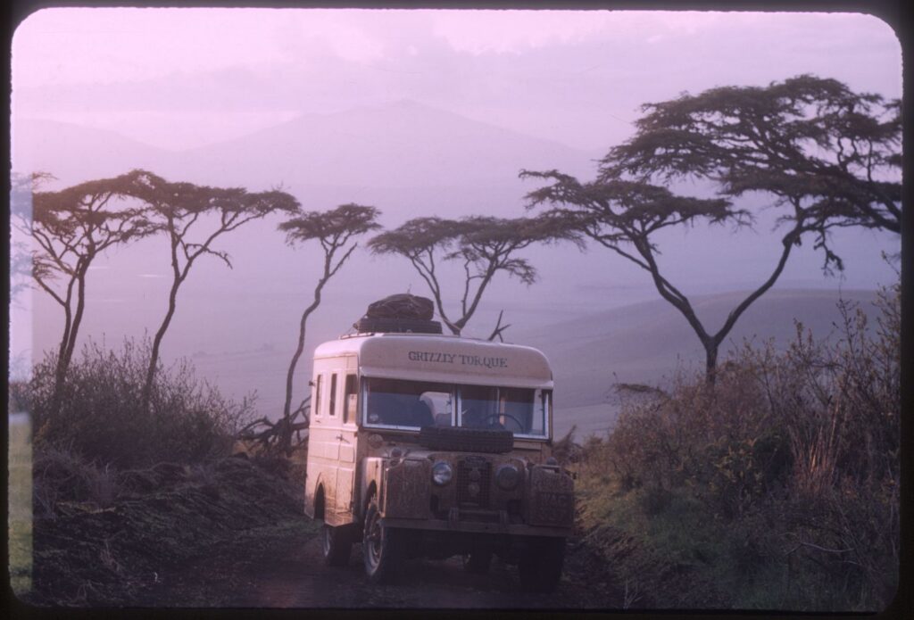 An archival photo of a white Land Rover with the words Grizzly Torque painted in black sits parked in an African safari at dusk.