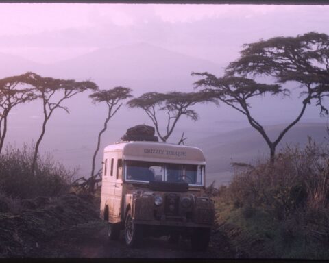 An archival photo of a white Land Rover with the words Grizzly Torque painted in black sits parked in an African safari at dusk.