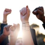 Hands, fist and students with protest outdoor for education riot, university equality and change law. Group, people and power with call to action for free learning, society support and racism justice stock photo