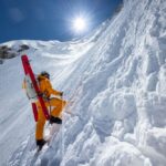 A mountain climer wearing a bright yellow suit ascends a snowy peak on Everest.