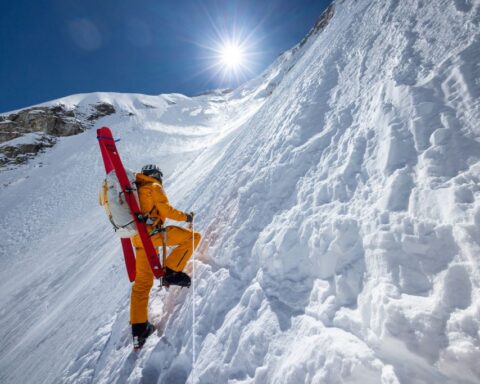 A mountain climer wearing a bright yellow suit ascends a snowy peak on Everest.