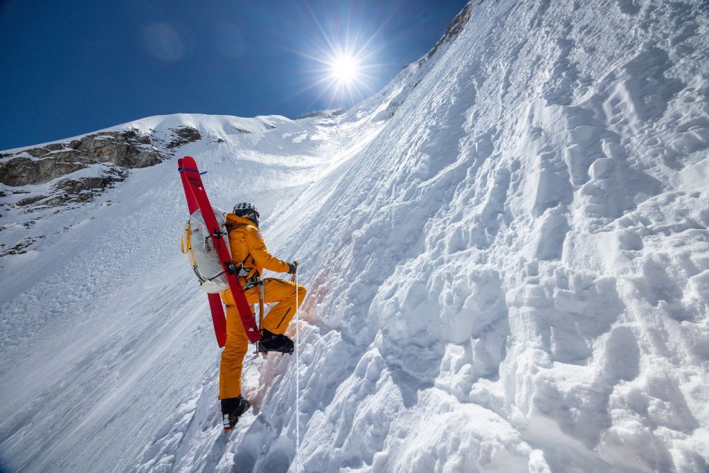 A mountain climer wearing a bright yellow suit ascends a snowy peak on Everest.