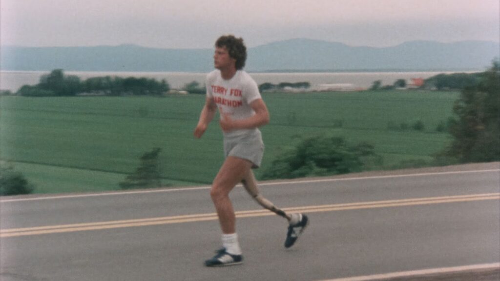 An archival image shows Terry Fox running along a rural street, wearing a white t-shirt and jogging shorts.