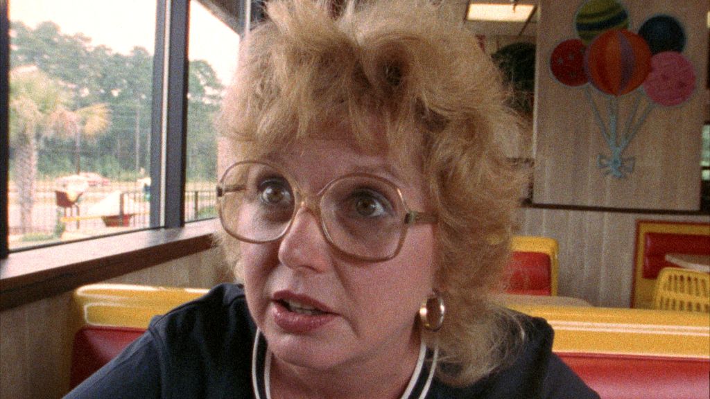 A close-up image shows Charleen Swansea in the film Sherman's March. She is a white woman with blond hair, expressive eyes, and big plastic glasses. The image is from the early 1980s and reflects the style of the time.