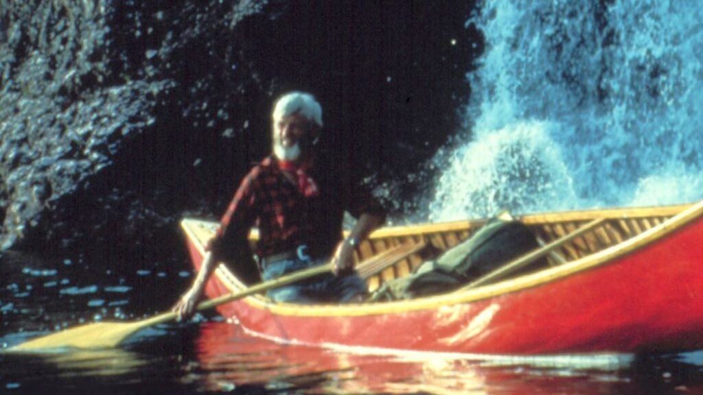 An archival image shows a man rowing a red canoe through a river.