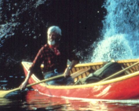 An archival image shows a man rowing a red canoe through a river.