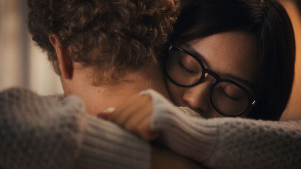 A Filipina woman with black glasses wmbraces her white partner. They are pictured in close-up.