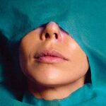 An Iranian woman is pictured in close up, lying beneath a teal surgical sheet. The sheet covers her body, with a hole cut that exposes her face from the nose to her chin.