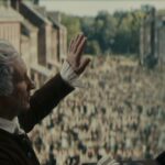Two men in Civil War era America speak before a crowd of people. The men have white wigs and black robes.