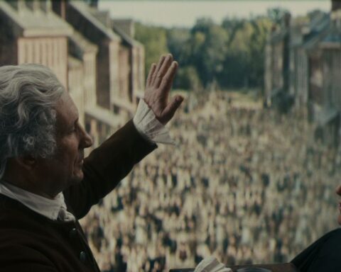 Two men in Civil War era America speak before a crowd of people. The men have white wigs and black robes.