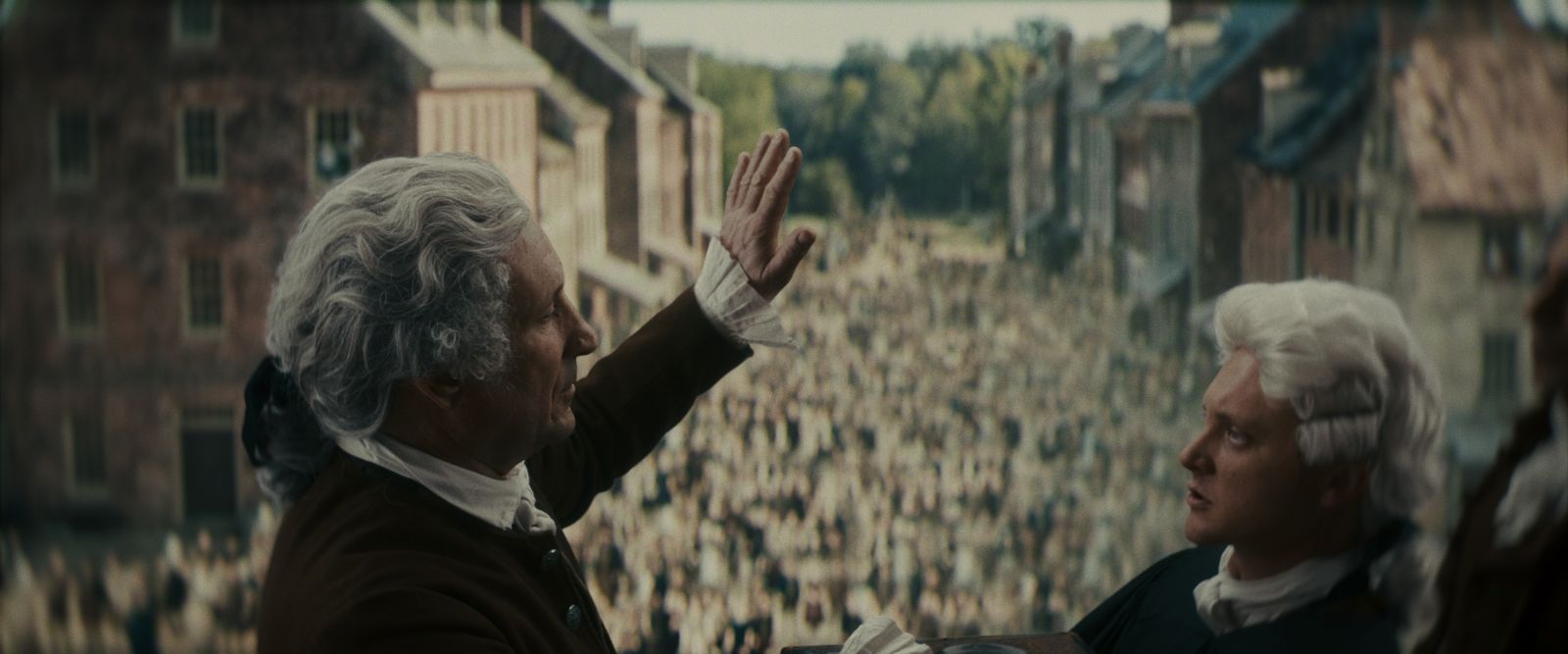 Two men in Civil War era America speak before a crowd of people. The men have white wigs and black robes.